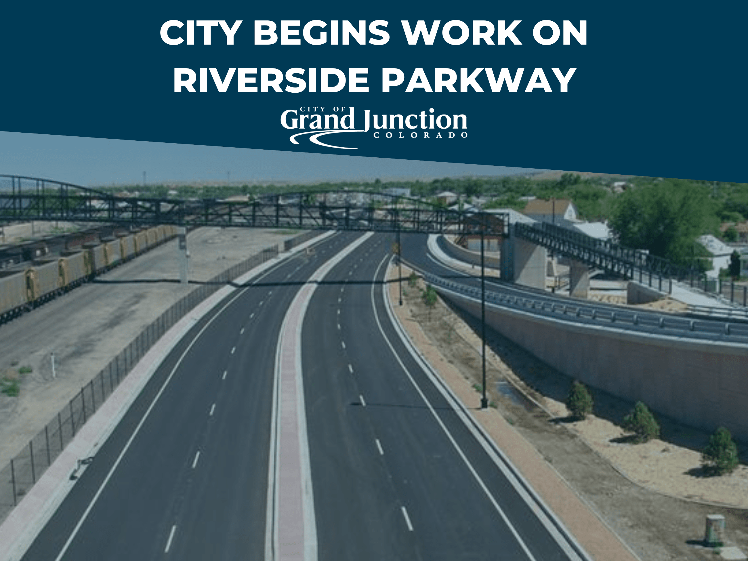 Ariel view of a roadway with train cars on one side and a pedestrian bridge above the road.