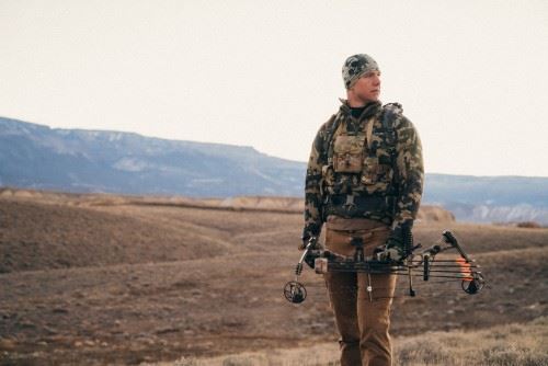 Man standing in a barren field holding a bow and arrows