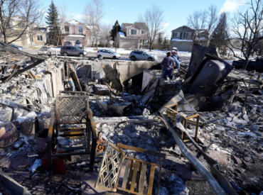 Ruble left after a fire/ people standing within ruble