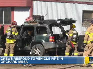 Firefighters standing around a vehicle that was on fire but is now put out