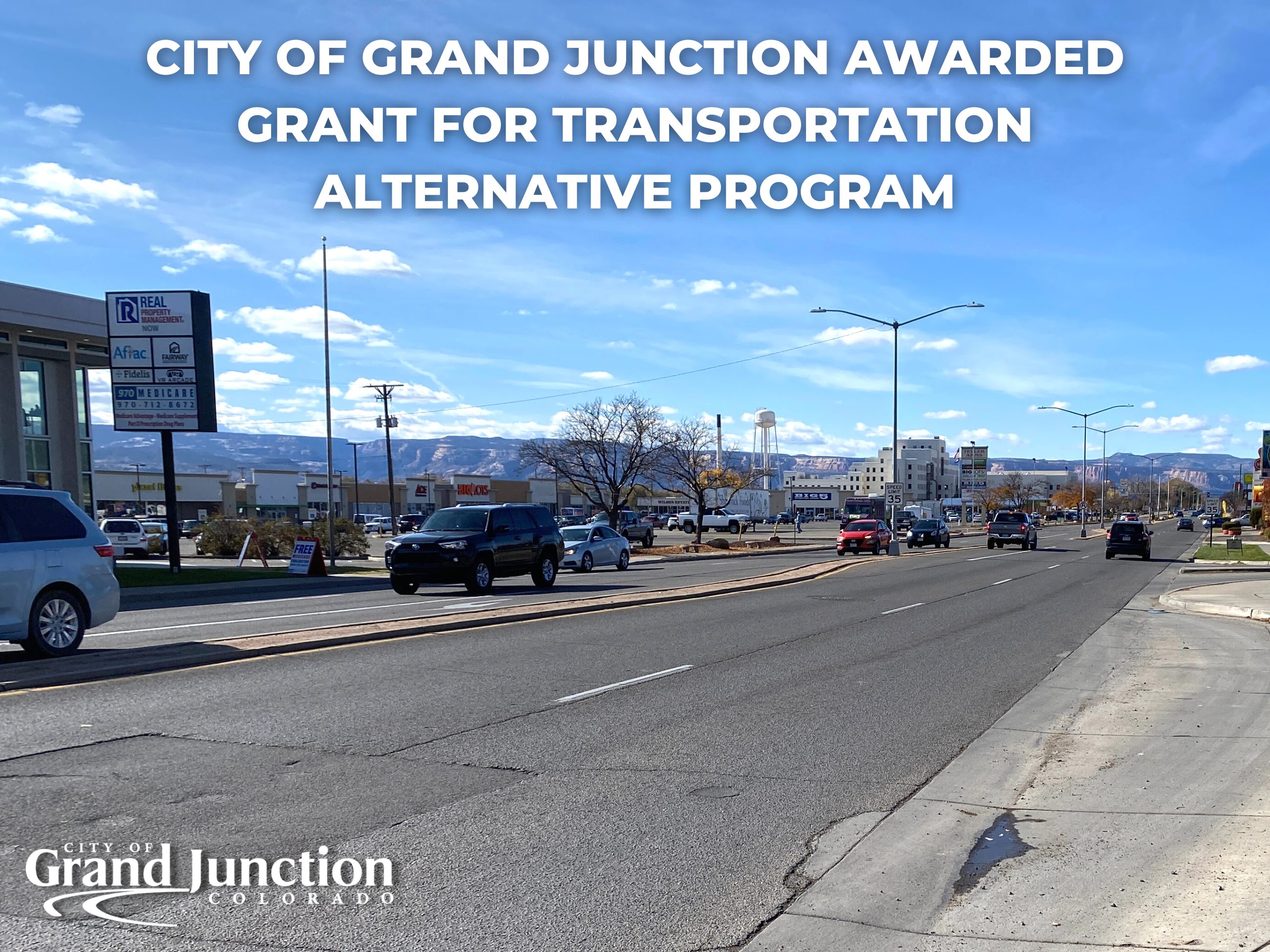 Street with cars traveling east and west. Sky and mountains in the background. 